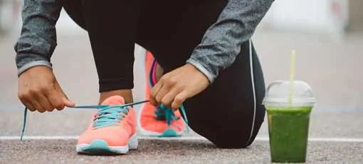 Sportlerin bindet sich die Schuhe - Smoothie steht auf dem Boden
