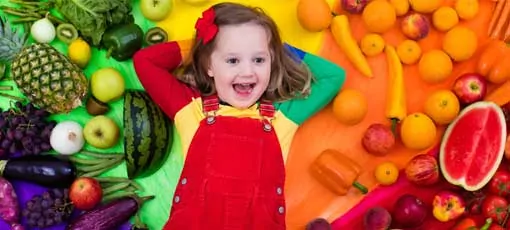 Bunt angezogenes Kind liegt zwischen Obst und Gemüse
