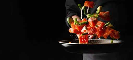 Diätkoch - professioneller Koch bereitet roten Fisch, Lachs, Forelle mit Gemüse zu.Kochen Meeresfrüchte, gesunde vegetarische Speisen und Essen auf dunklem Hintergrund.