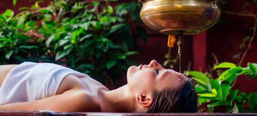 Fernlehrgang: Ayurvedische Diagnostik - Ayurveda Massage alternative Heiltherapie.Schönes, kaukasisches Weibchen, das eine Shirodhara-Behandlung erhält, liegt auf einem Holztisch im indischen Salon